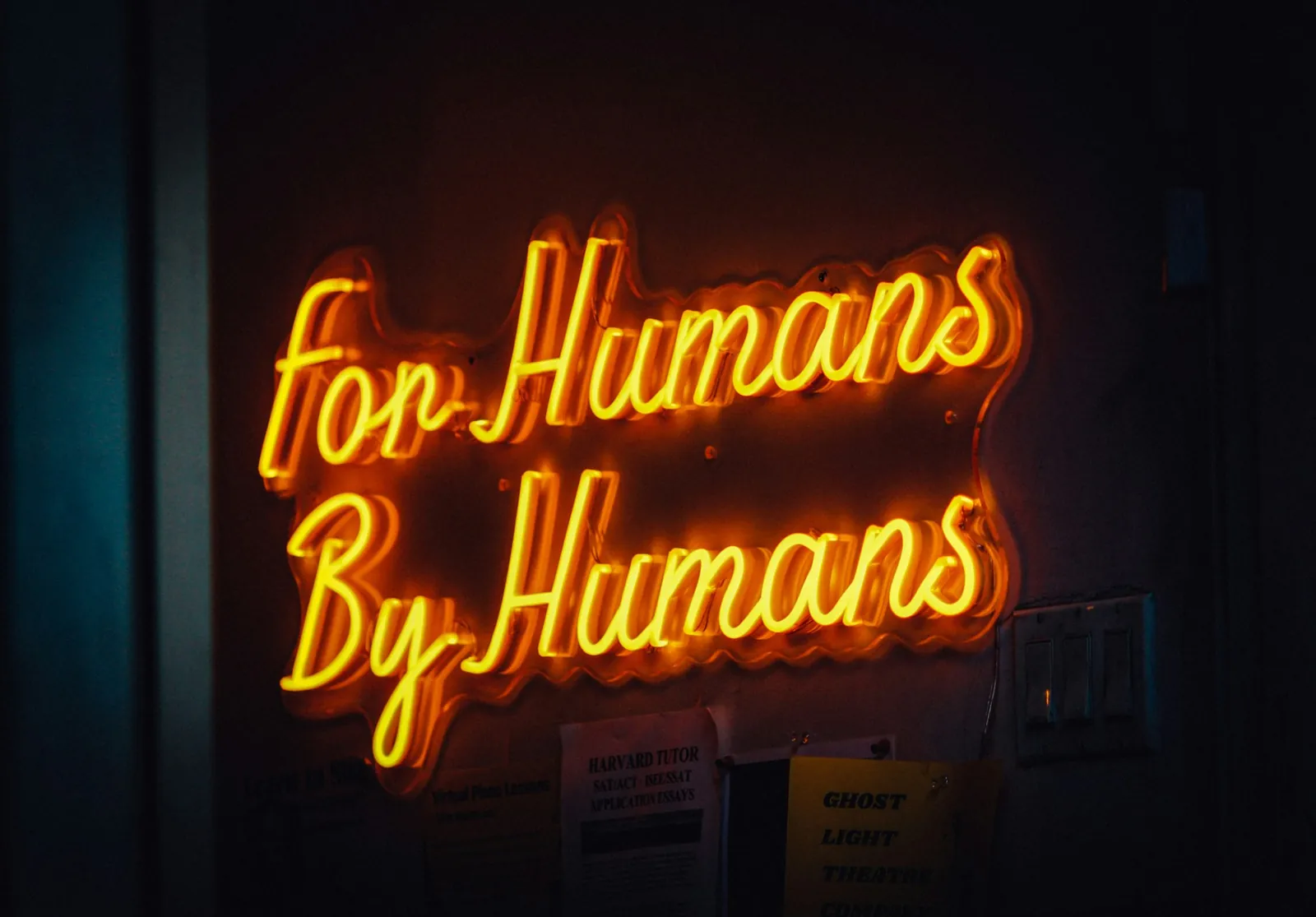 A warm neon sign reading For Humans By Humans on a dark wall